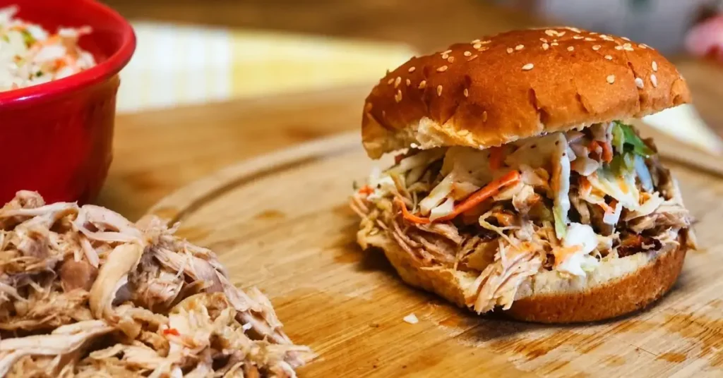 Tangy Carolina pulled chicken sandwich topped with coleslaw on a sesame bun served on a wooden cutting board.