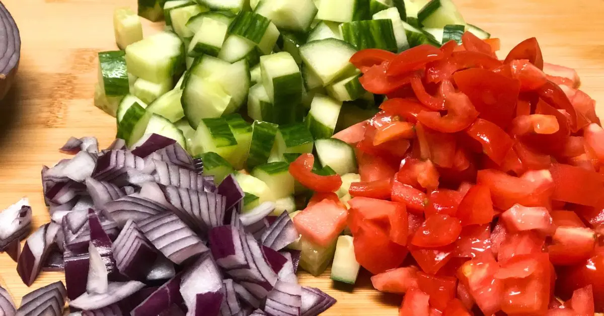 Finely diced cucumber, Roma tomatoes, and red onion for authentic Israeli salad.