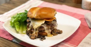 garlic parmesan turkey burger with lots of cheese and mushrooms beside a bed of lettuce on a white plate