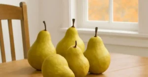A few pears on a table with a view of a fall-colored tree with orange leaves outside the window.