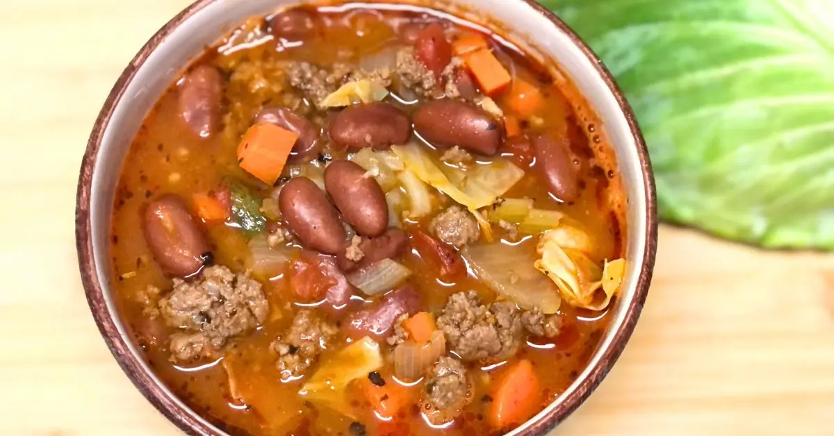 Shoney’s copycat cabbage soup served in a teal bowl with fresh cabbage on a wooden board