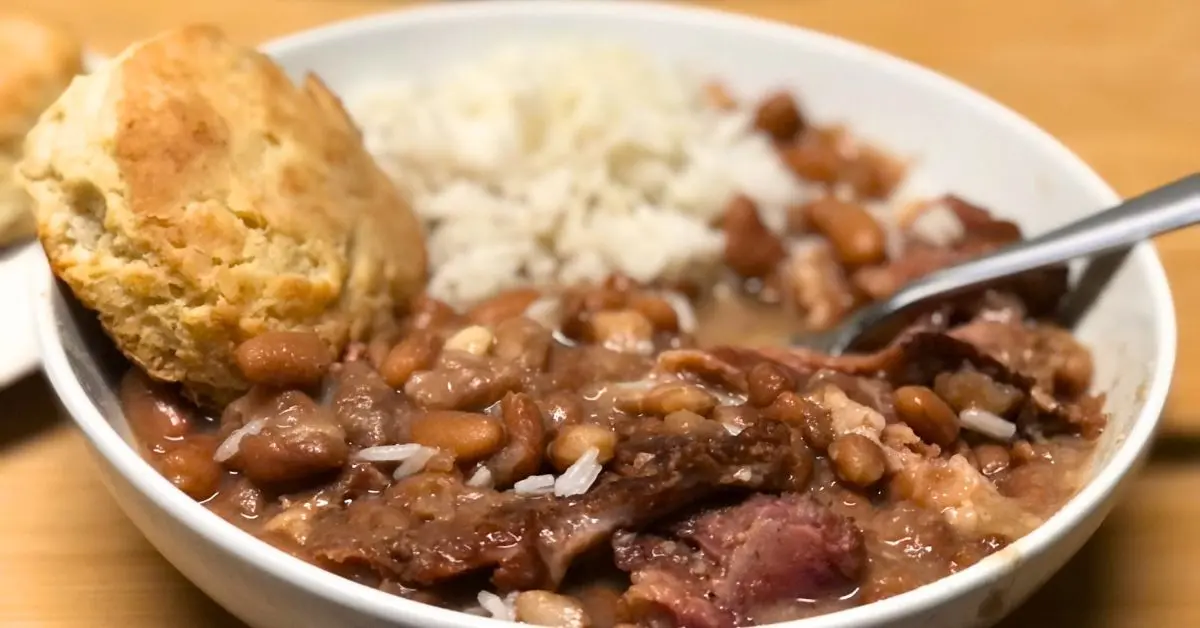 Hearty Southern-style pinto beans with chunks of smoked meat, served in a bowl with a golden buttery biscuit and a small mound of white rice.