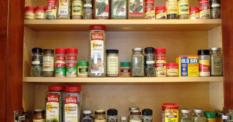 An open kitchen cabinet filled with various spice bottles and containers.