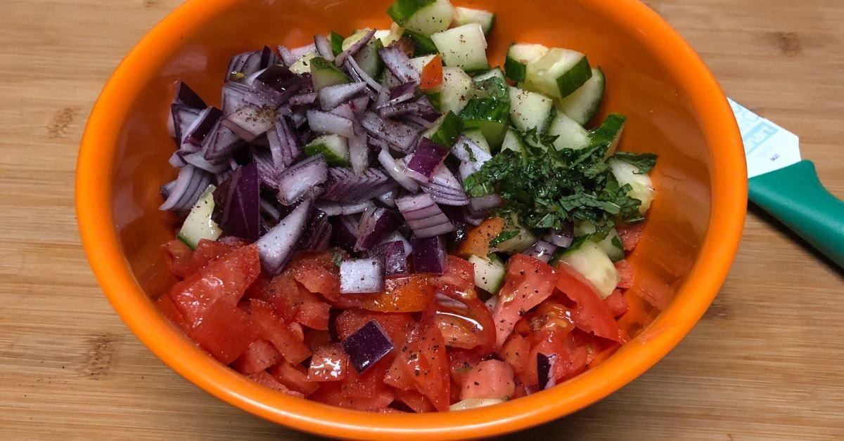 Chopped cucumber, tomatoes, red onion, mint, and sumac in a bowl before mixing for Israeli salad recipe.