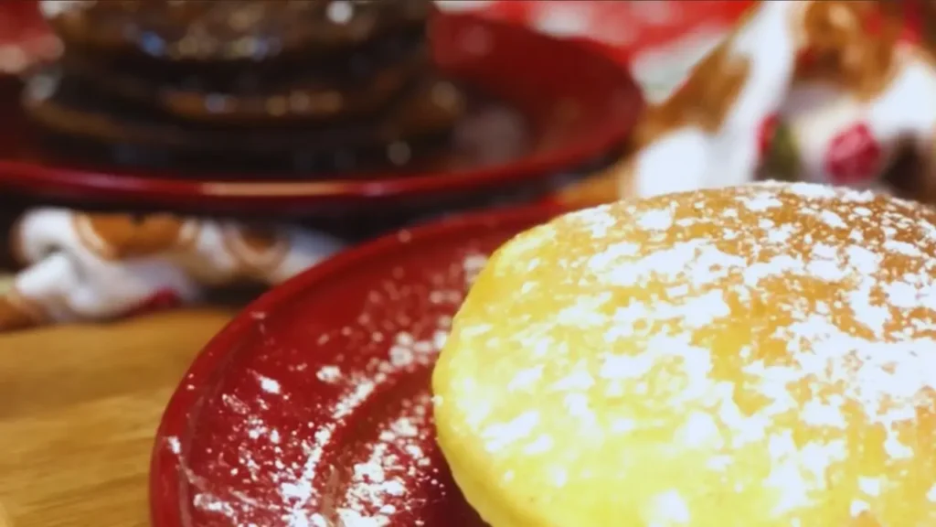 Stacked pancakes on a plate with powdered sugar: eggnog pancakes in front, gingerbread pancakes with molasses syrup in the back.