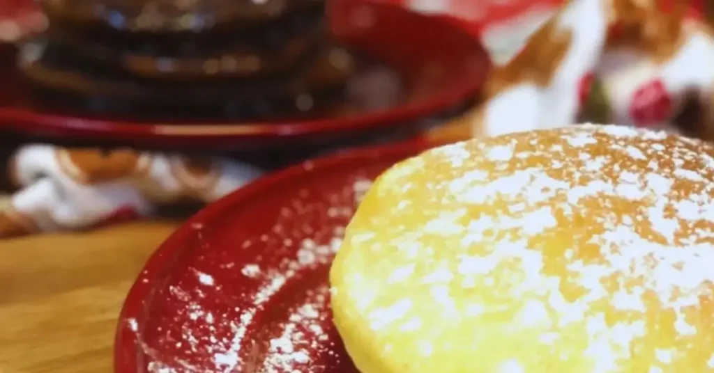 Stacked pancakes on a plate with powdered sugar: eggnog pancakes in front, gingerbread pancakes with molasses syrup in the back.