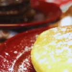 Stacked pancakes on a plate with powdered sugar: eggnog pancakes in front, gingerbread pancakes with molasses syrup in the back.