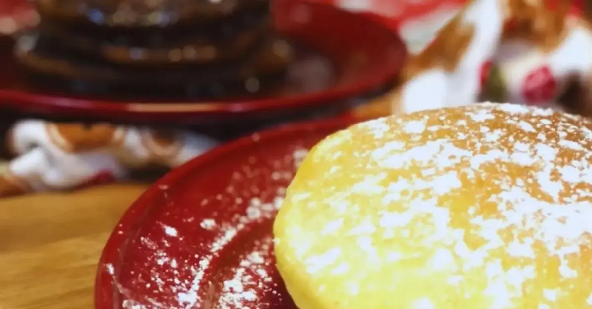 Stacked pancakes on a plate with powdered sugar: eggnog pancakes in front, gingerbread pancakes with molasses syrup in the back.