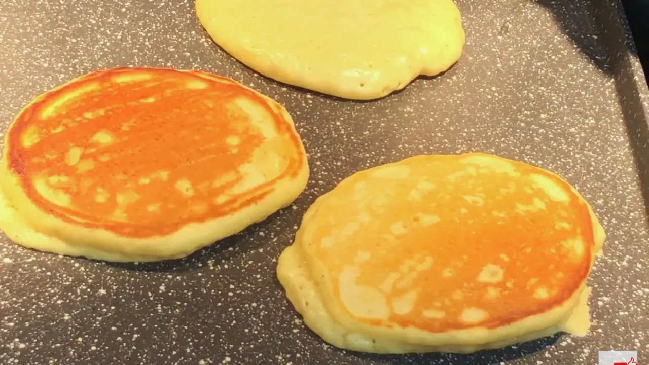 Eggnog pancakes cooking on a griddle, some flipped to golden brown and others not yet flipped.