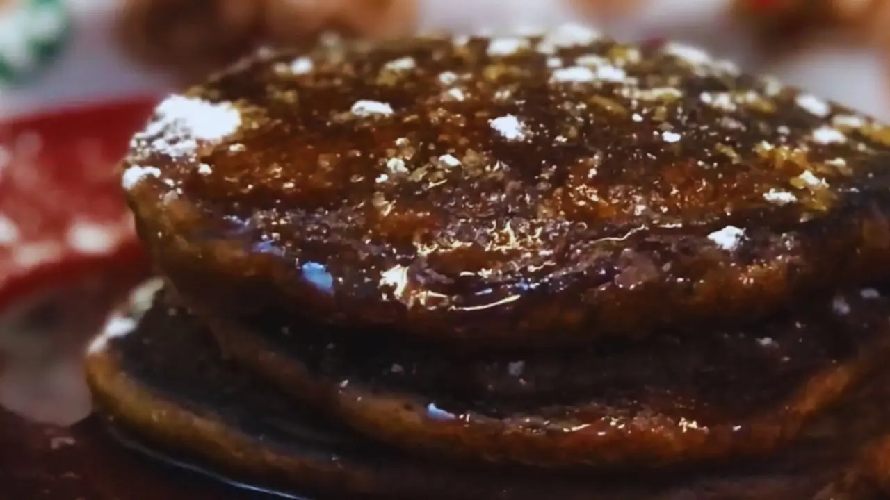 Stacked gingerbread pancakes on a red plate, drizzled with molasses syrup and sprinkled with powdered sugar.