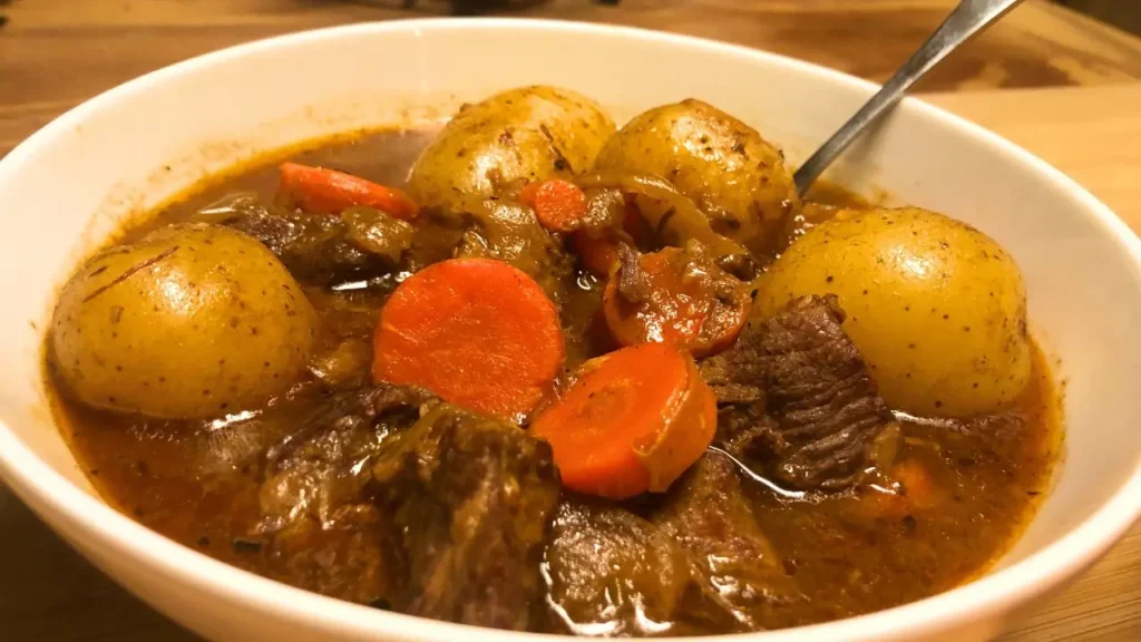 Hearty beef stew without wine in a white bowl with large chunks of chuck roast, whole baby gold potatoes, sliced carrots, and flavorful broth.