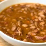 Italian bean stew made with dried beans, ham bone, and bacon served in a white bowl with rustic bread