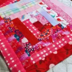a bright and colorful log cabin quilt block in reds, dark pinks and light blues and pinks.
