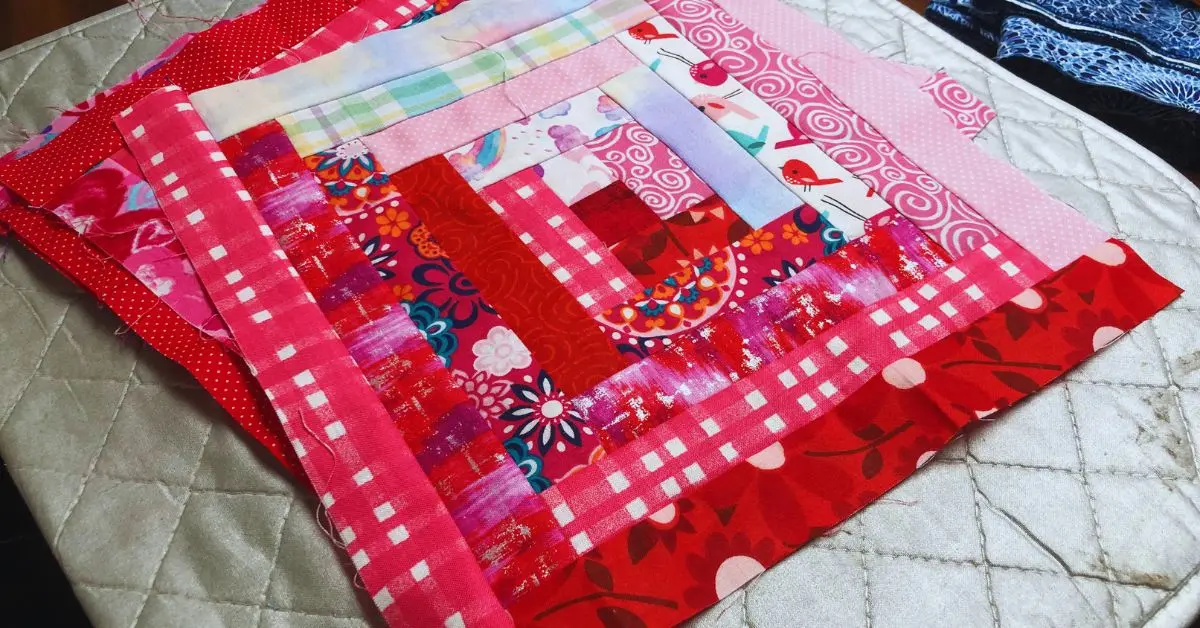 a bright and colorful log cabin quilt block in reds, dark pinks and light blues and pinks.