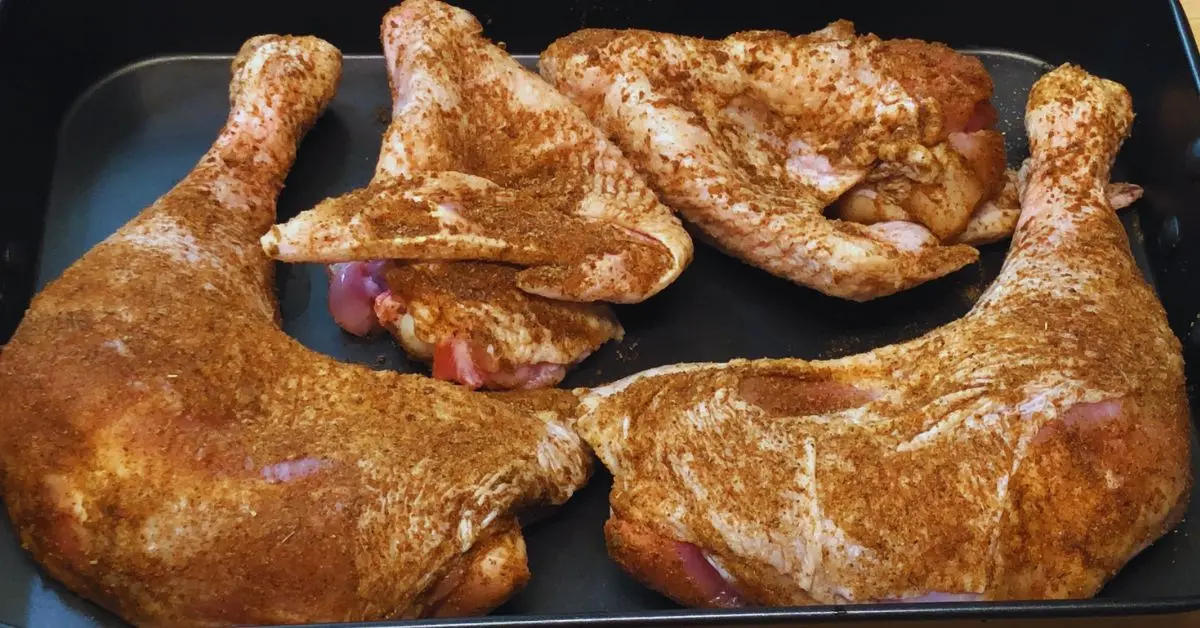 raw turkey leg quarters and wings covered in seasoning.