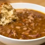 Hearty bean soup with ham in a white bowl topped with crusty bread, one of 5 easy soup recipes I make on repeat for family dinners.