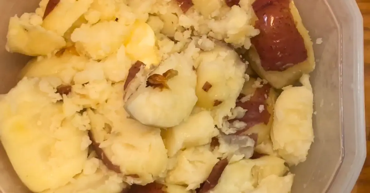 Cooked red potatoes in a bowl with butter and roasted garlic before mashing