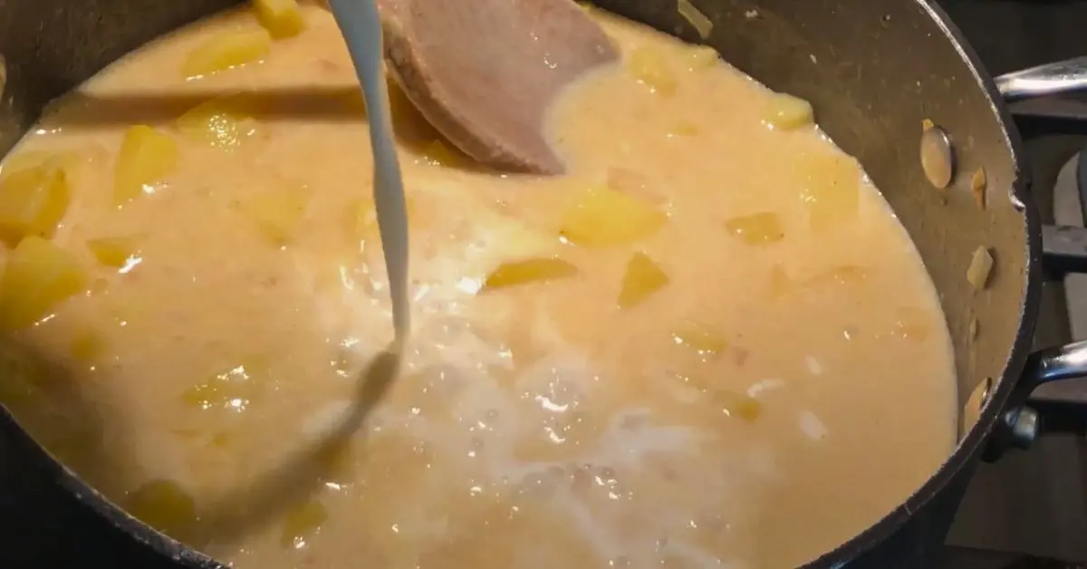 Potatoes simmering in a pot with milk being added for creamy potato soup