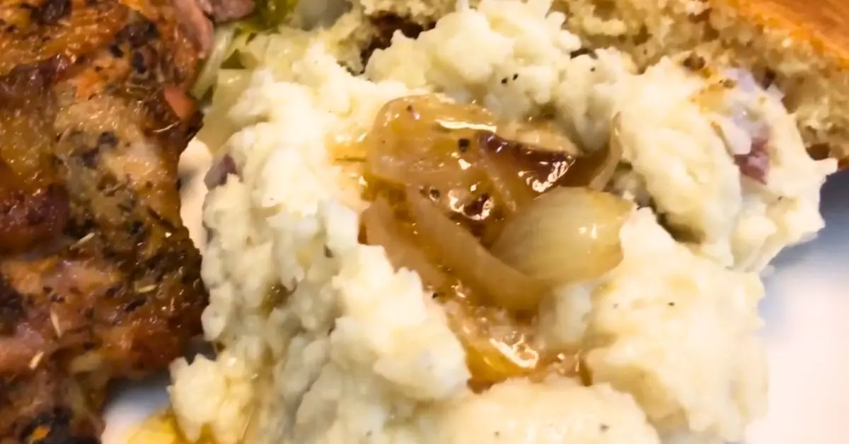 Red skinned mashed potatoes with buttered onions, baked chicken, and cornbread on a dinner plate