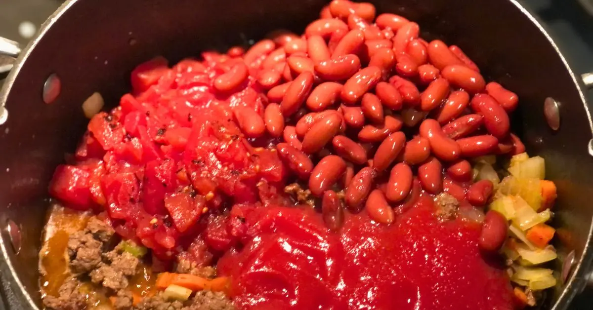 Kidney beans, diced tomatoes, and tomato sauce layered on top of the cooked beef and vegetables in a pot for Shoney’s cabbage soup.