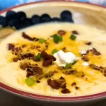 Bowl of simple creamy potato soup topped with cheddar cheese, sour cream, crispy bacon, and chopped green onions