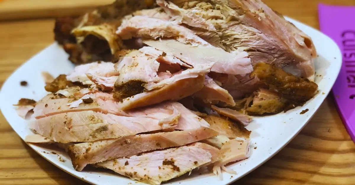 smoked turkey plate that one side has been chopped up sits on white plate on wooden table