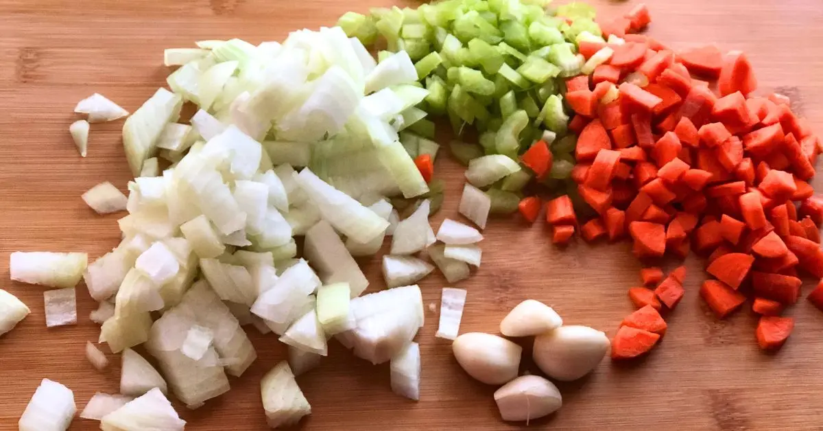 Chopped carrots, onions, celery, and four cloves of garlic arranged in a large wooden bowl for Shoney’s cabbage soup.
