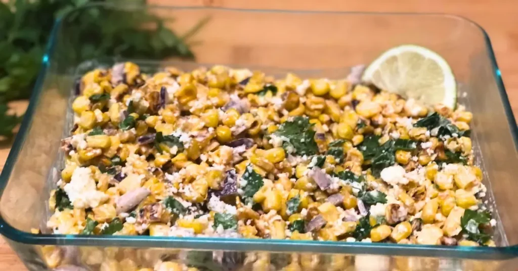 harred Mexican corn salad in a glass dish topped with lime with fresh cilantro on a wooden board