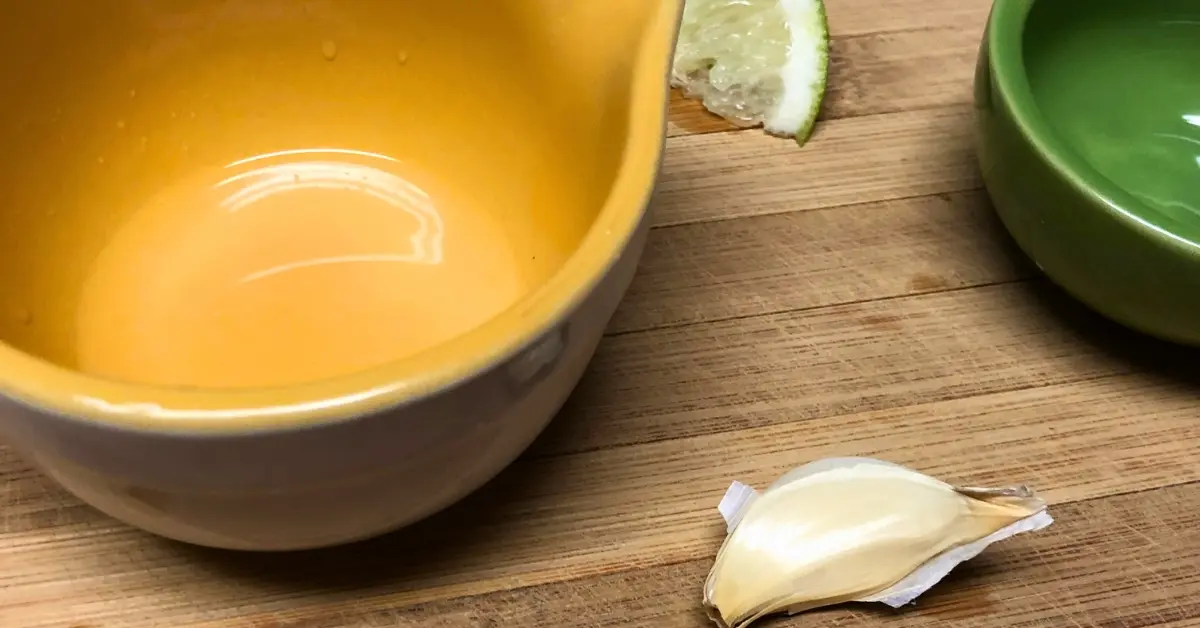 Garlic clove and fresh lime juice in a small bowl on a wooden board