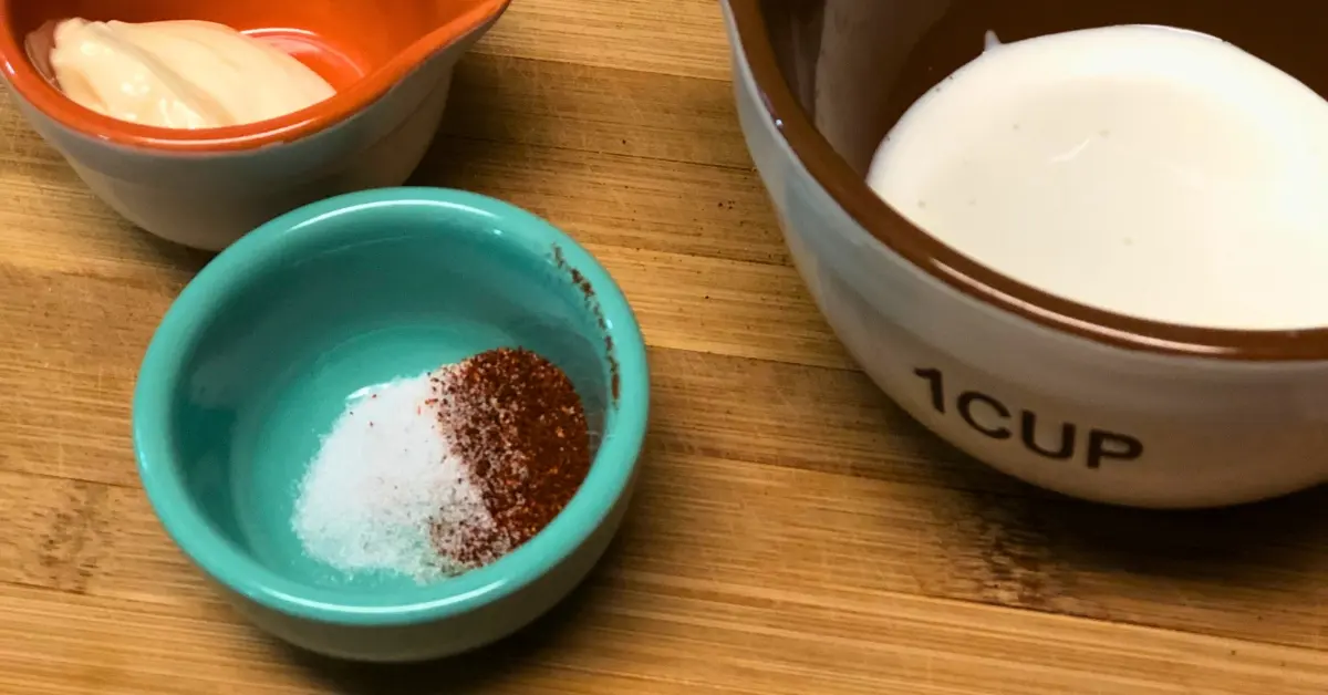 Small bowls of mayonnaise, cream, chili powder, and salt for Mexican corn salad dressing