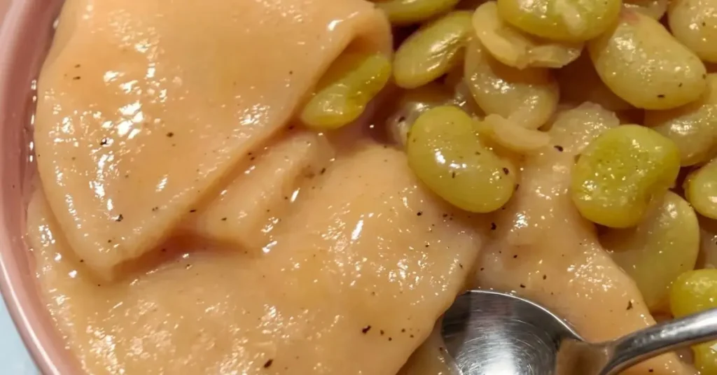 A beautiful, rustic close-up of tender, square-cut Southern flat dumplings simmered to perfection in a rich, velvety chicken broth, garnished with freshly cracked black pepper and a hint of baby lima beans in a ceramic bowl.