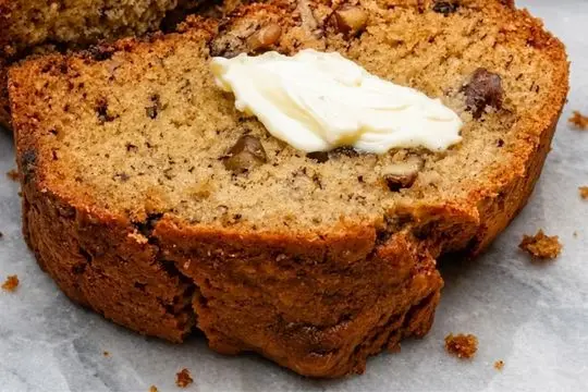 Moist all butter banana bread with one slice cut and topped with butter.