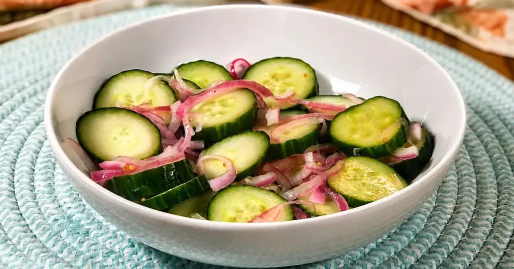 Cucumber salad with quick pickled red onions in a tangy vinegar brine served in a white bowl.