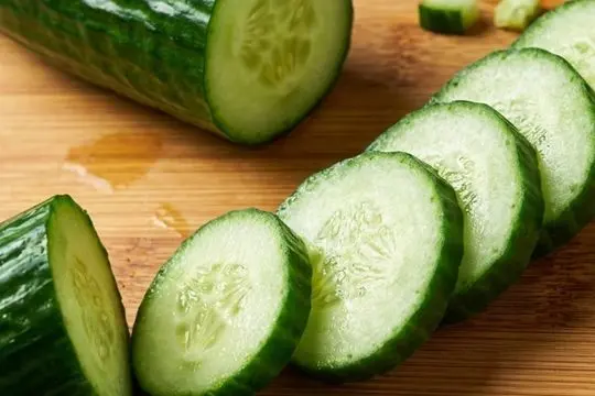 Crisp, green English cucumber slices neatly arranged in a row alongside a halved cucumber on a wooden cutting board.
