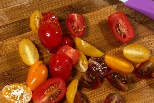 Close-up of sliced, fresh, red and yellow cherry tomatoes on a wooden cutting board.