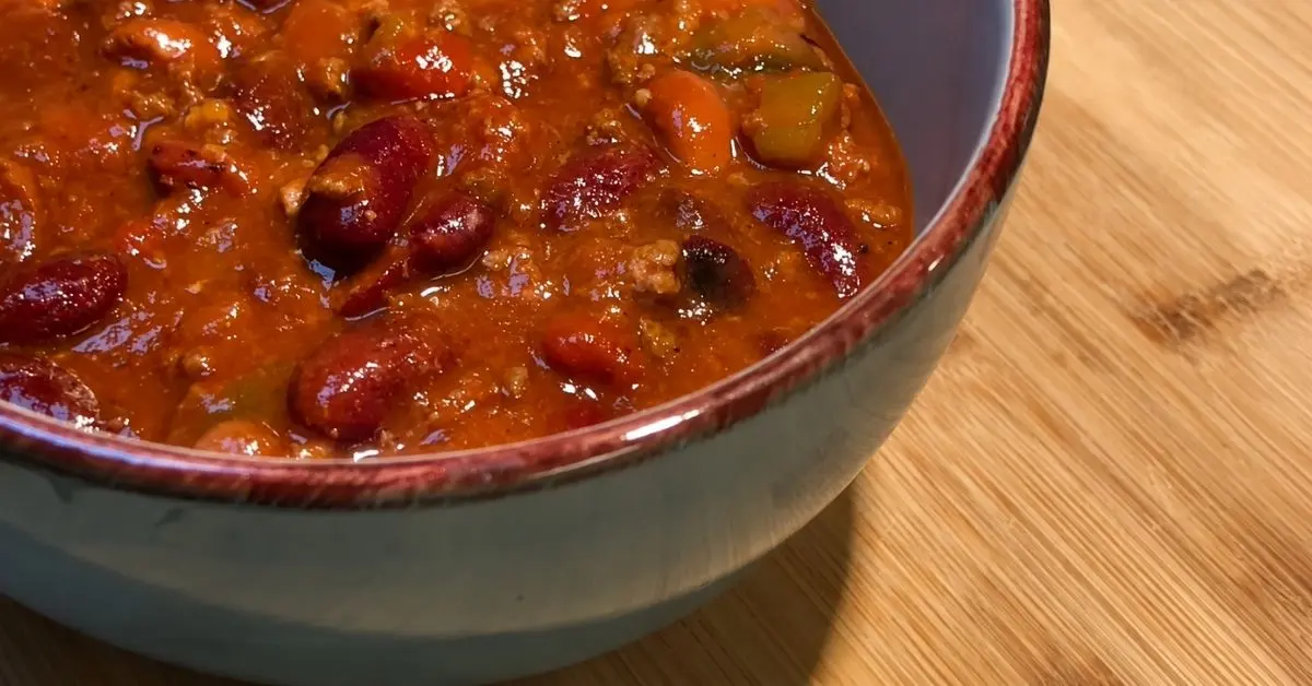 Homemade chili with kidney beans served in a teal bowl on a wooden board