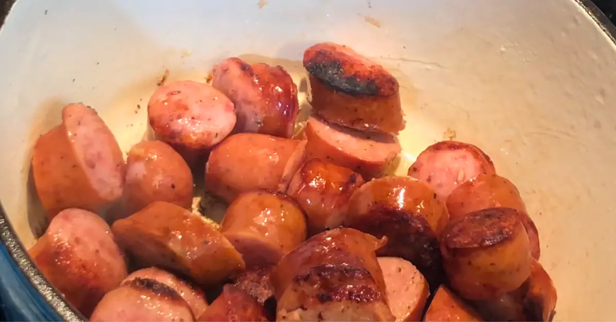 Sliced smoked sausage browning in a blue Dutch oven for split pea soup