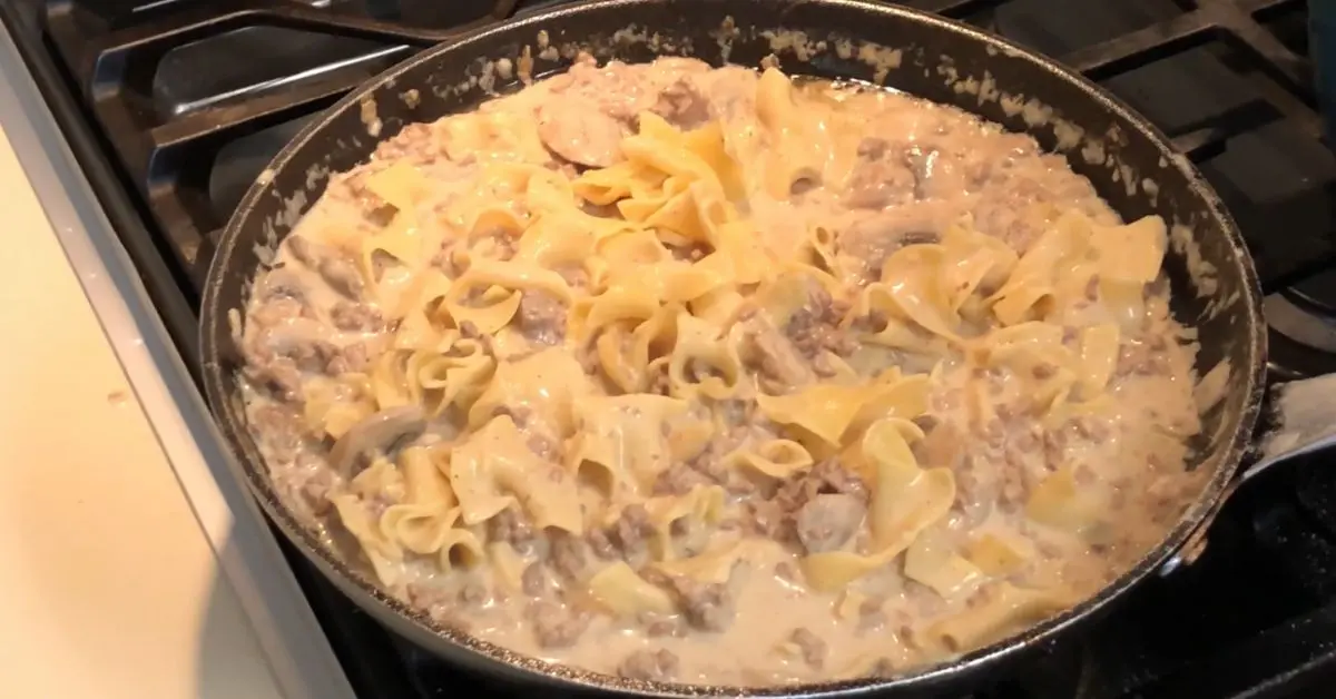 Egg noodles being added to the creamy ground beef stroganoff