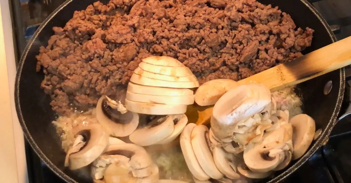Browned ground beef and cremini mushrooms cooking in a skillet