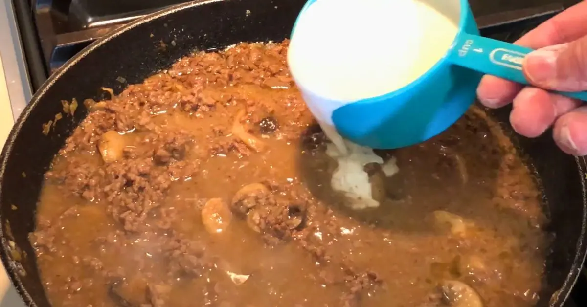 Heavy cream being added to the ground beef stroganoff sauce