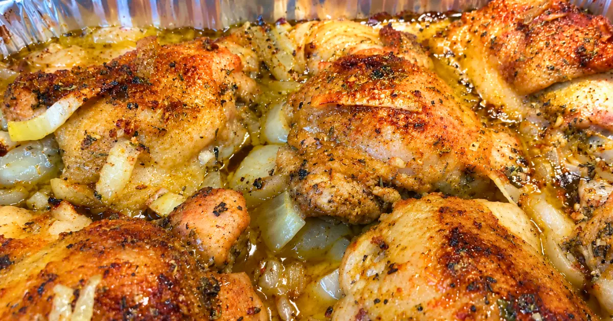 Golden baked chicken thighs in a pan with onions and broth.