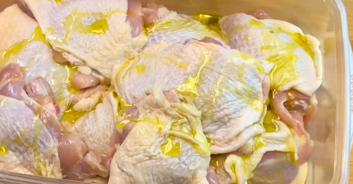 Raw chicken thighs in a baking pan drizzled with oil before seasoning.