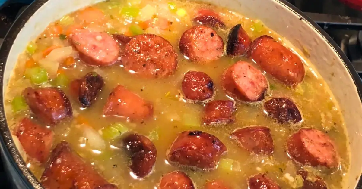 Sliced smoked sausage added to split pea soup in a Dutch oven