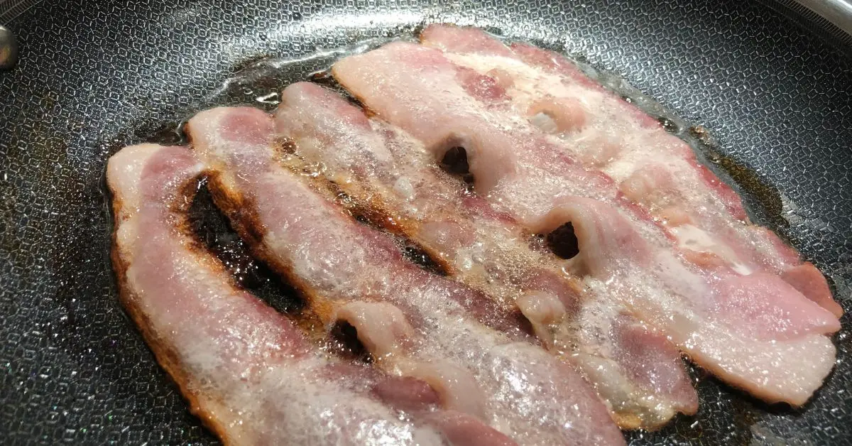Bacon sizzling in a skillet to render fat for beanie weenies