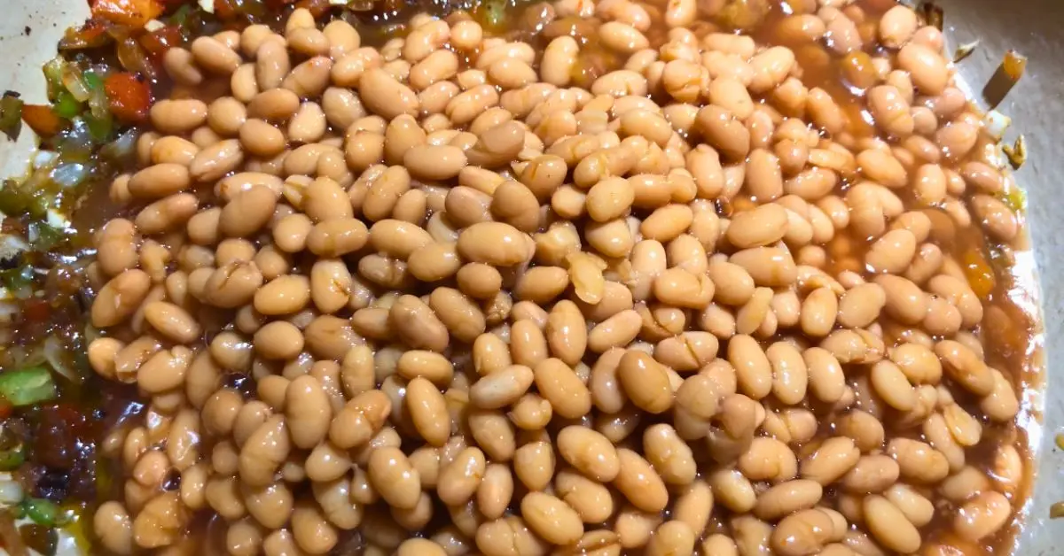 Close up of pork and beans and sauted bell peppers and onions in a dutch oven