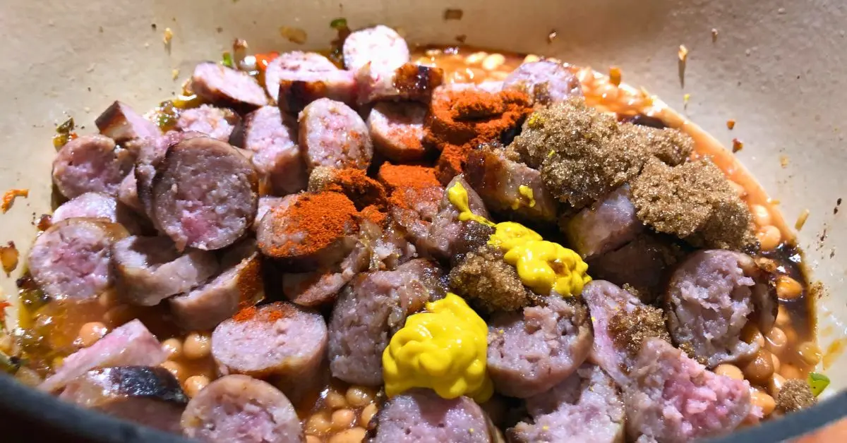 Sliced sausage and pork and beans topped with mustard and paprika before cooking