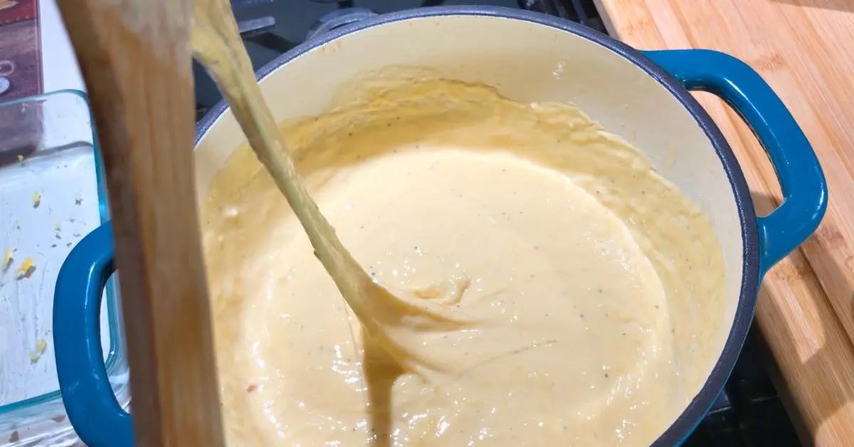 Creamy melted cheese sauce stretching from a wooden spoon in a teal Dutch oven