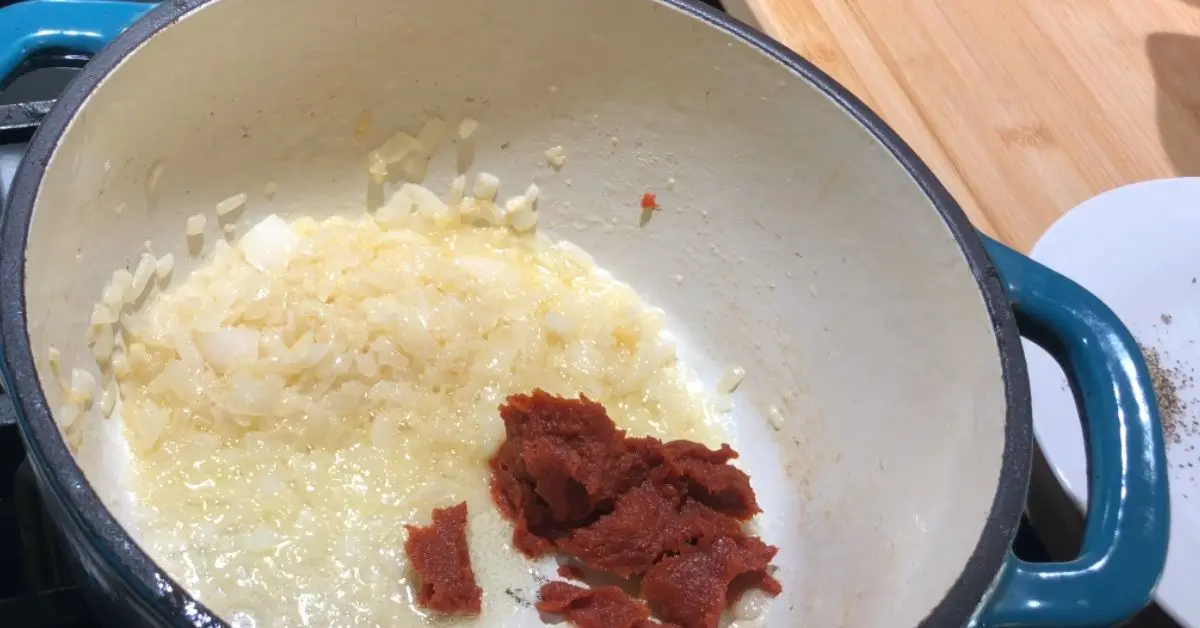 Onions, garlic, and tomato paste sautéing in a pot for creamy Parmesan tomato soup