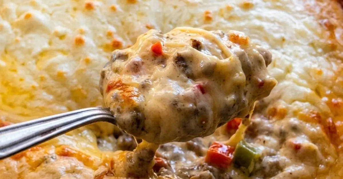 Steak-umm Philly cheesesteak dip with melted cheese served by the spoonful in front of a glass baking dish