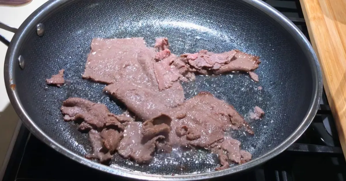 Thinly sliced Steak-umm beef browning in a skillet for Philly cheesesteak dip